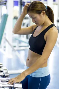 women in sports bra gets ready to pickup dumbbells in a gym.